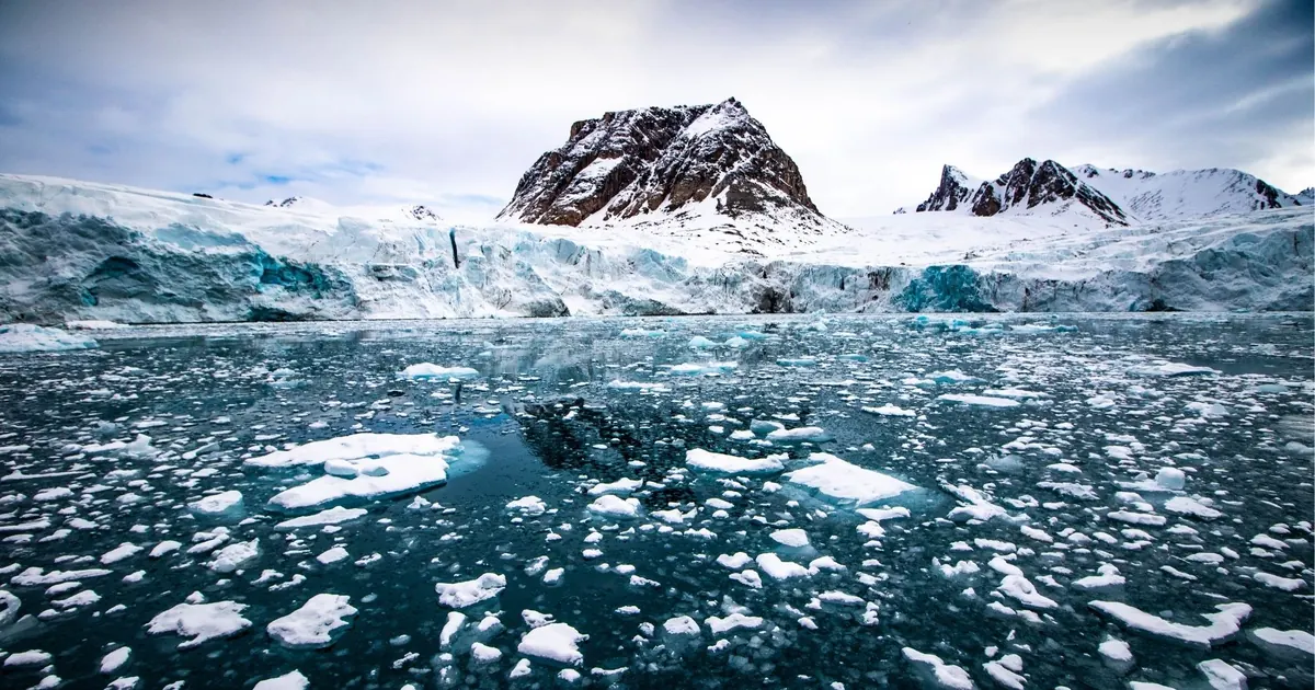 Broken glacier ice floating in a Svalbard fjord below a snow-covered peak