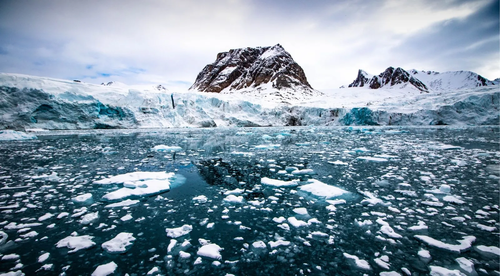 Glacier front and brash ice filling a Svalbard fjord beneath a dark rock summit