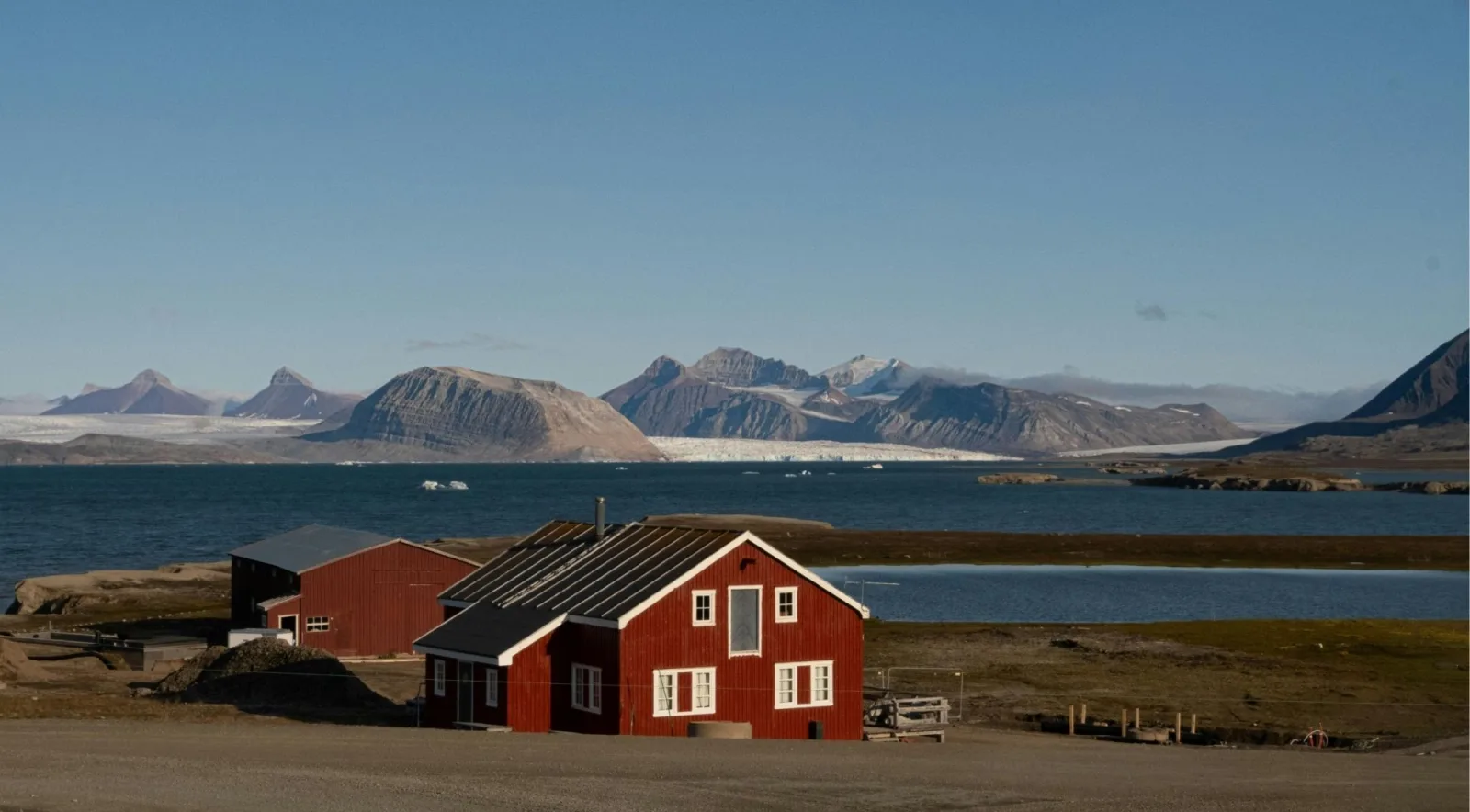 Red wooden research buildings on a Svalbard shoreline with a glacier across the fjord