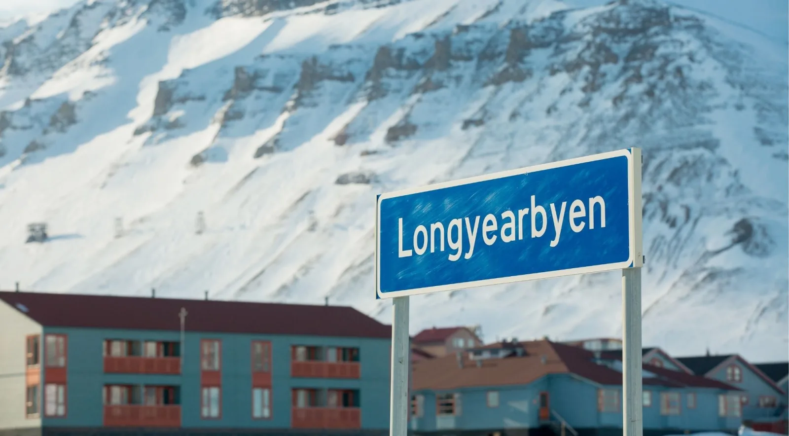 Blue Longyearbyen road sign in front of a snow-covered mountainside