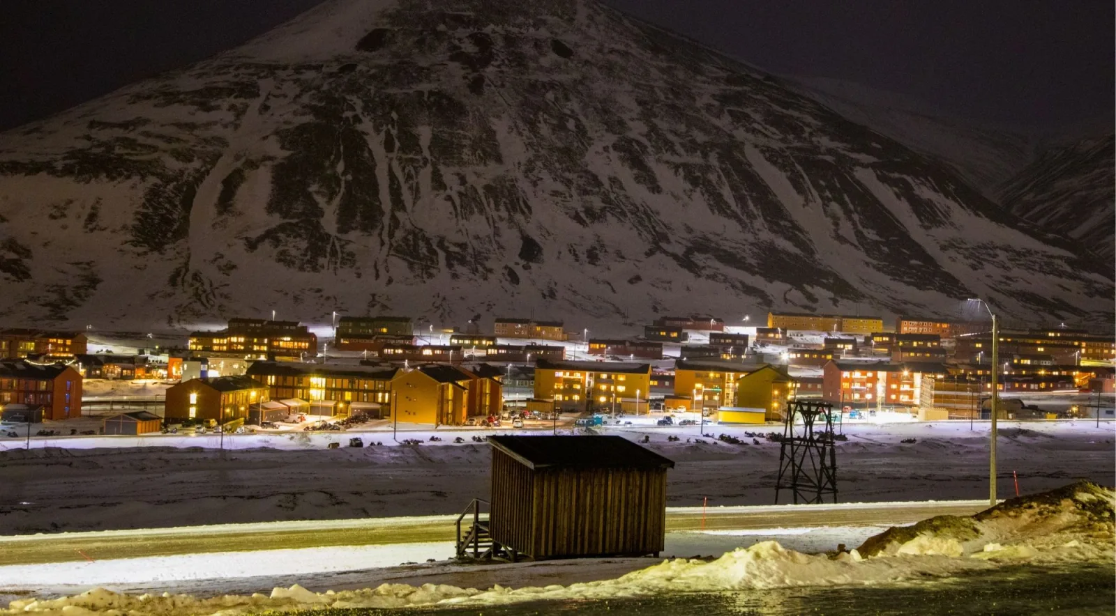 Longyearbyen lit up at night during the polar night, beneath a dark snow-covered mountain