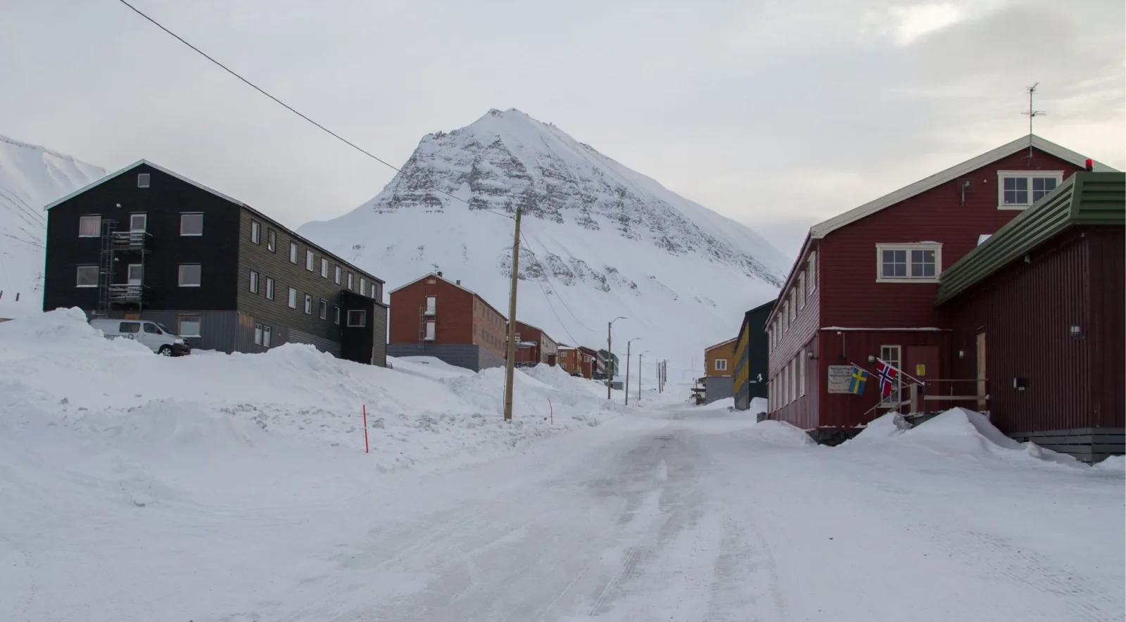 Snow-banked Longyearbyen street between timber buildings with a peak at the end
