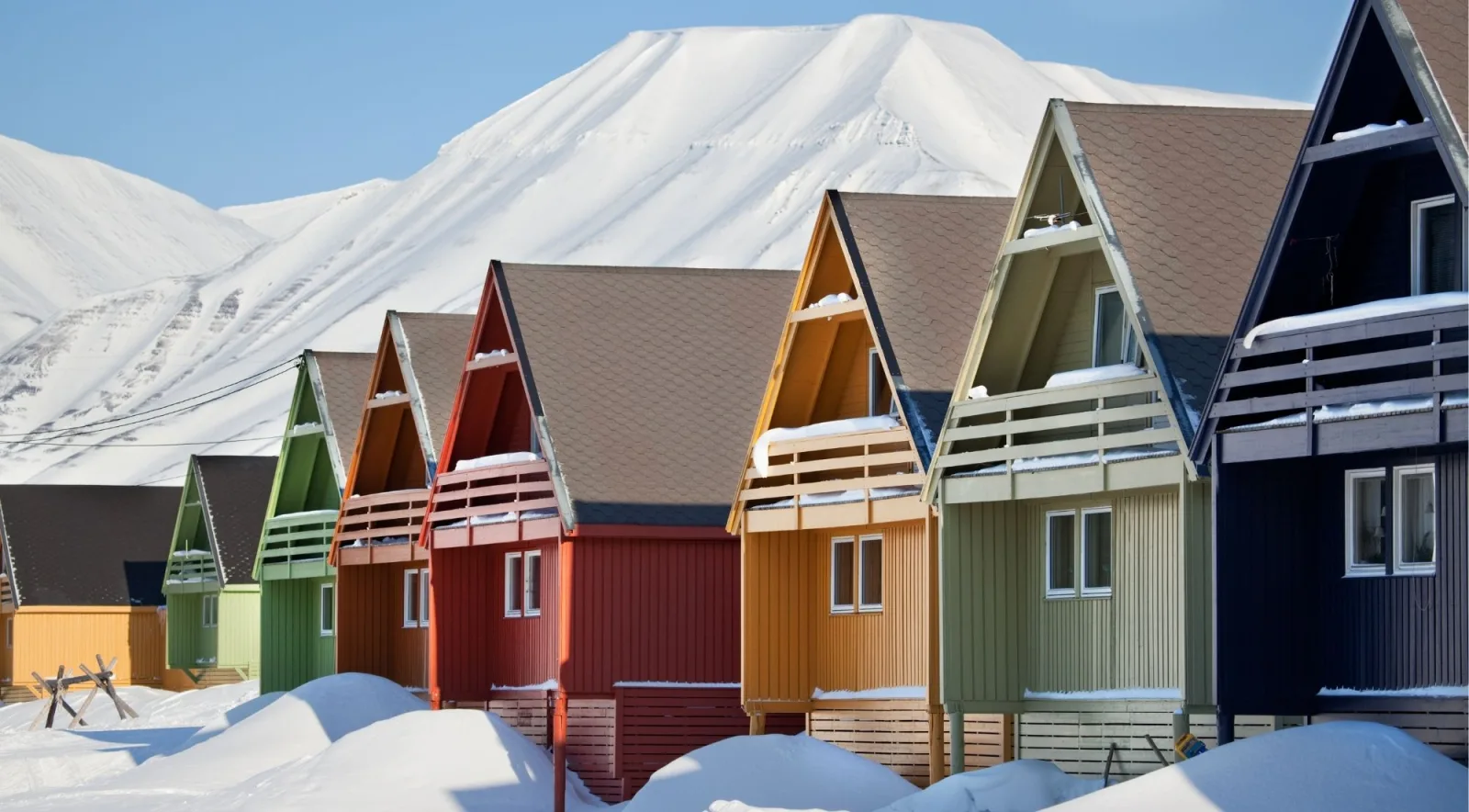 Bright row of red, green, orange and yellow A-frame houses under a snowy Longyearbyen peak