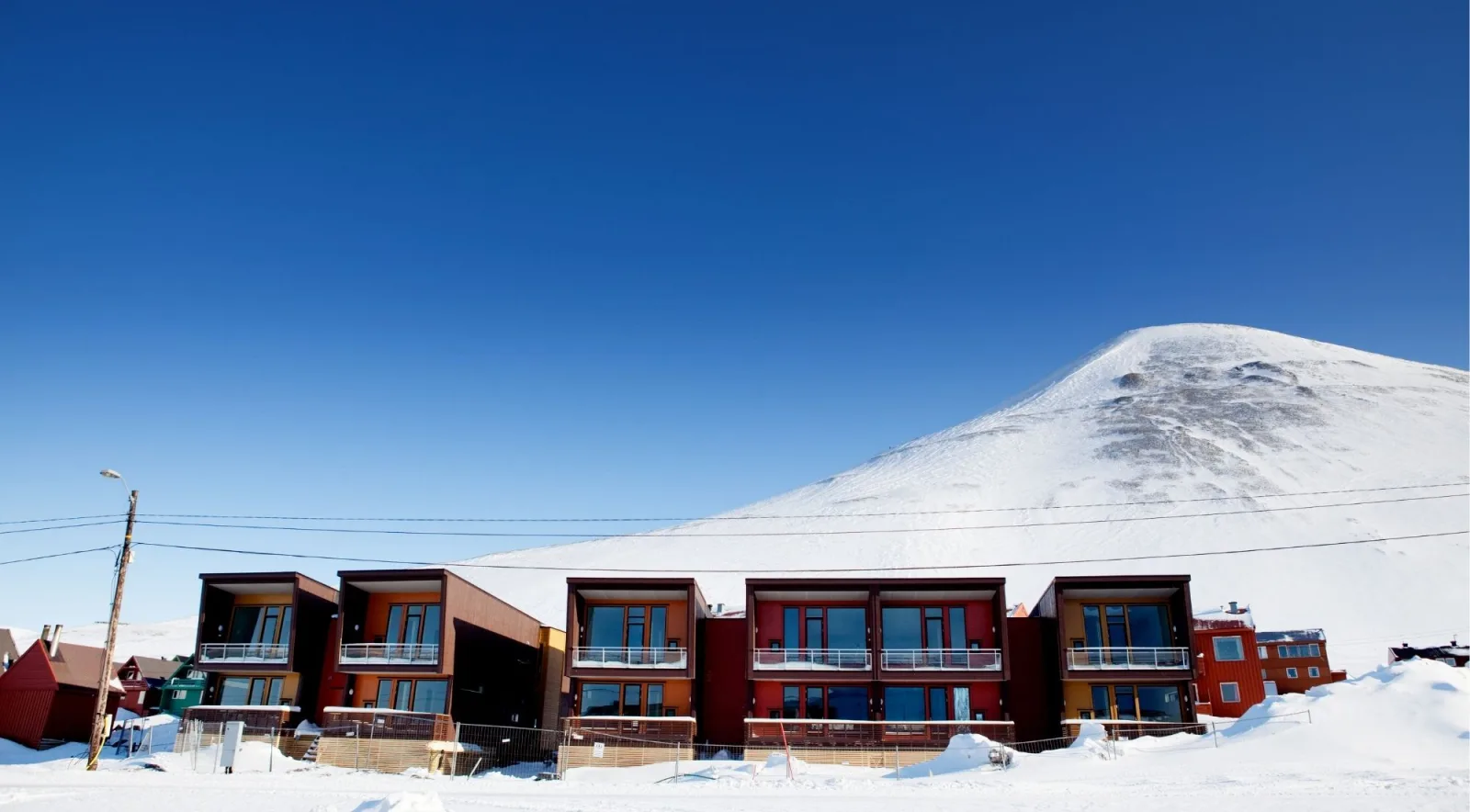 Modern timber apartment buildings in Longyearbyen beneath a snow-covered dome of a mountain