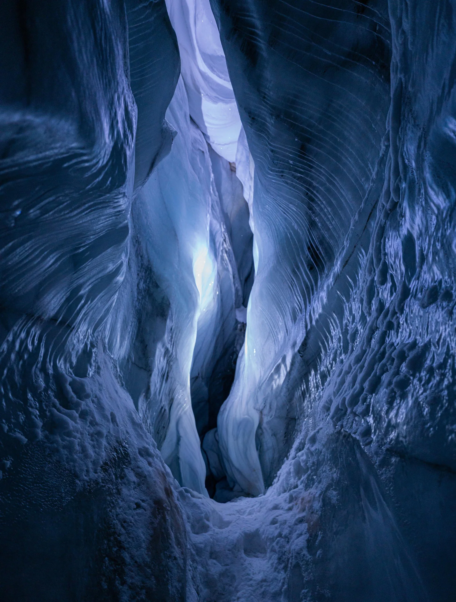 The blue banded walls of a Svalbard glacier ice cave narrowing to a lit crevasse above
