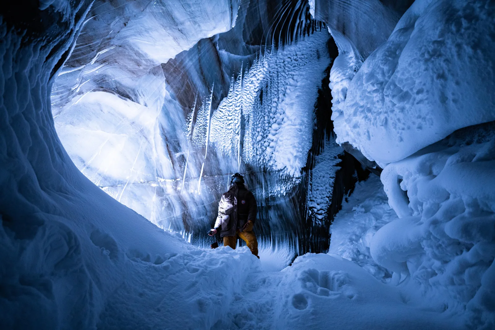 A visitor standing beneath frozen waterfalls in the blue chamber of a glacier ice cave