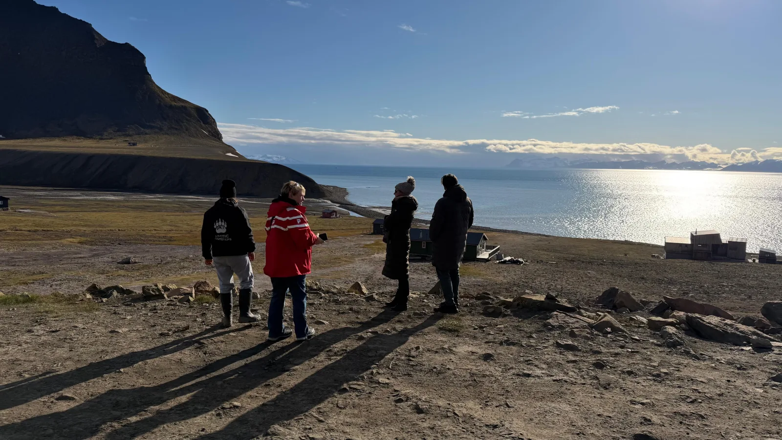 A small guided group on the Bjorndalen shore looking out over Isfjorden, low Arctic sun on the water