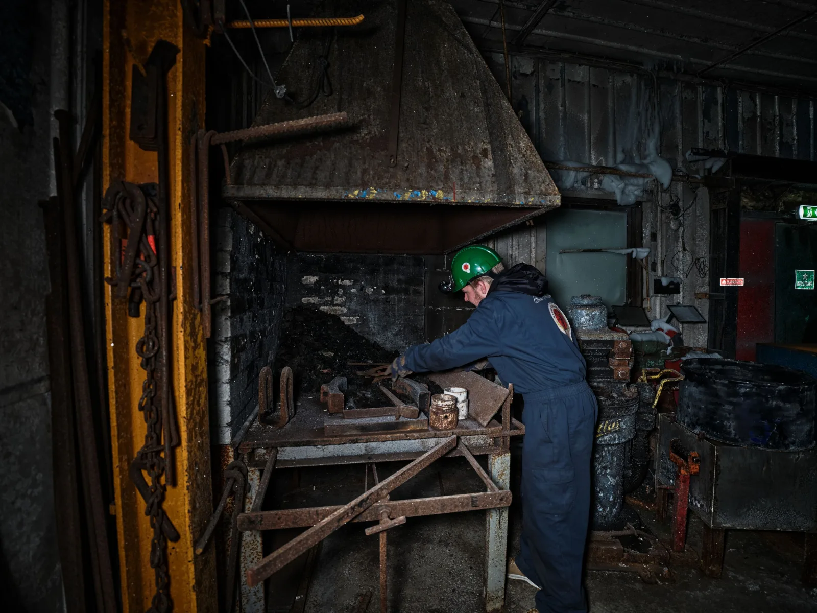 Guide working at the mine's forge, tools and chains hanging on the wall behind
