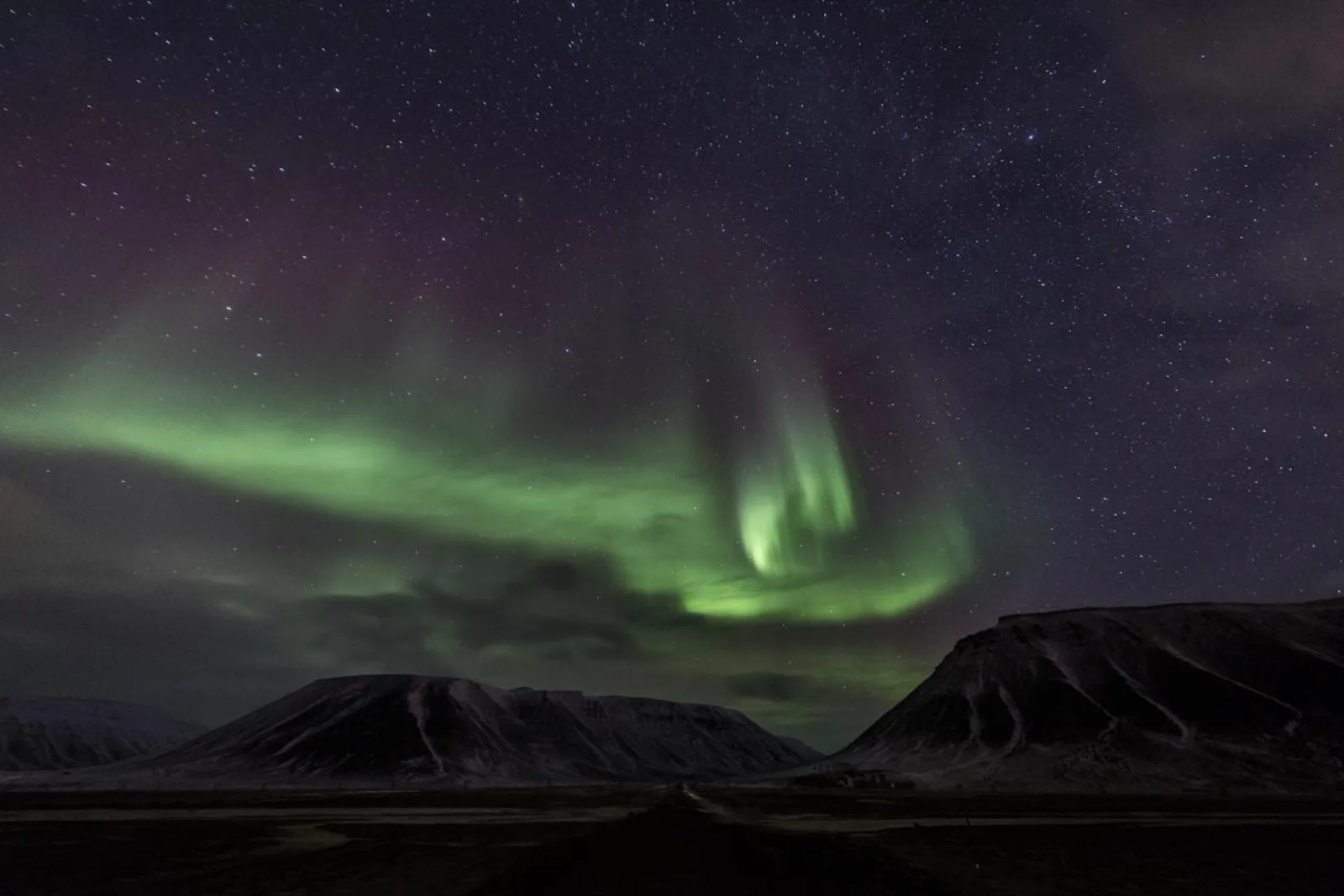 A broad green and violet aurora over the valley mouth outside Longyearbyen