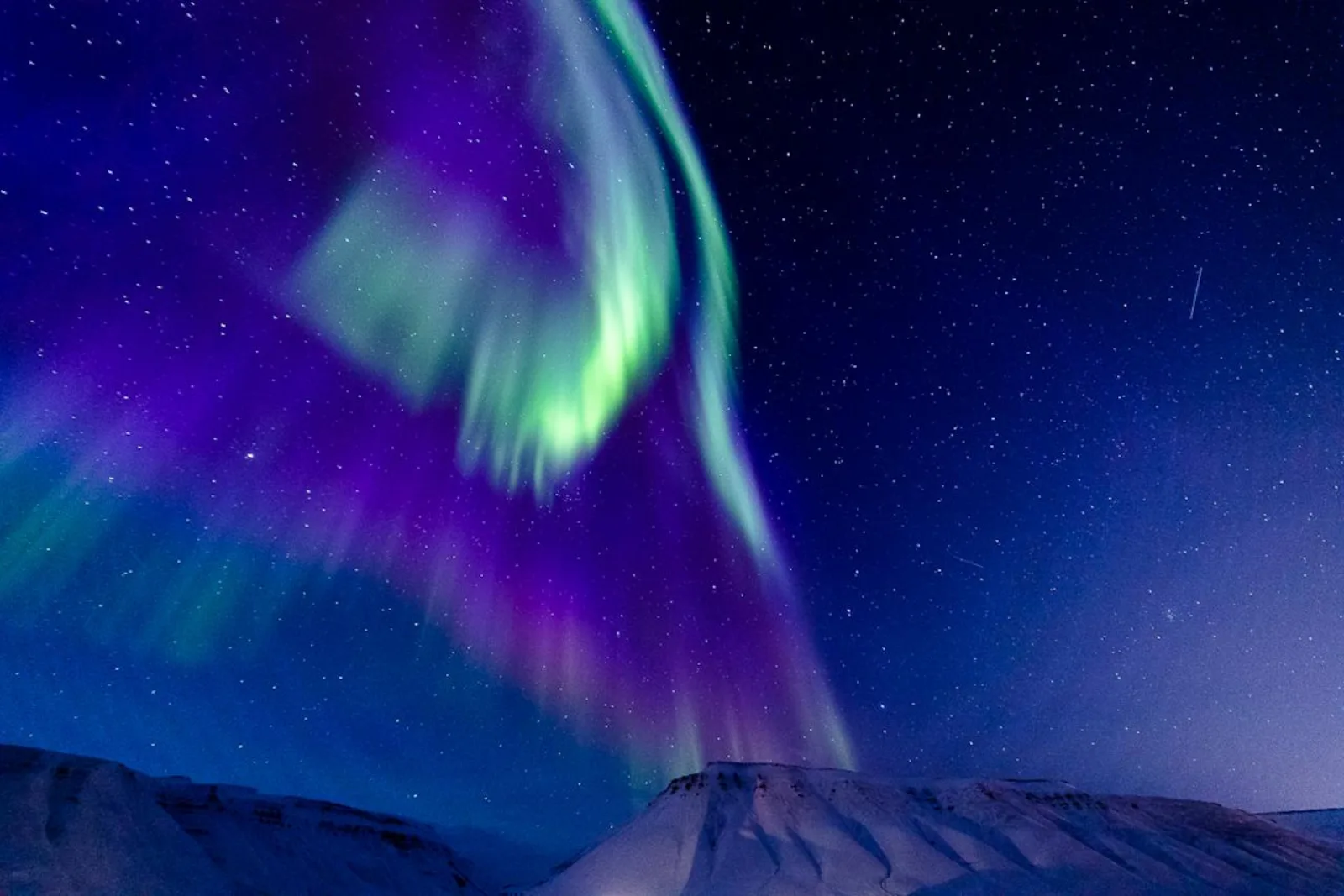 An intense green and purple aurora corona above a snow-covered Svalbard ridge