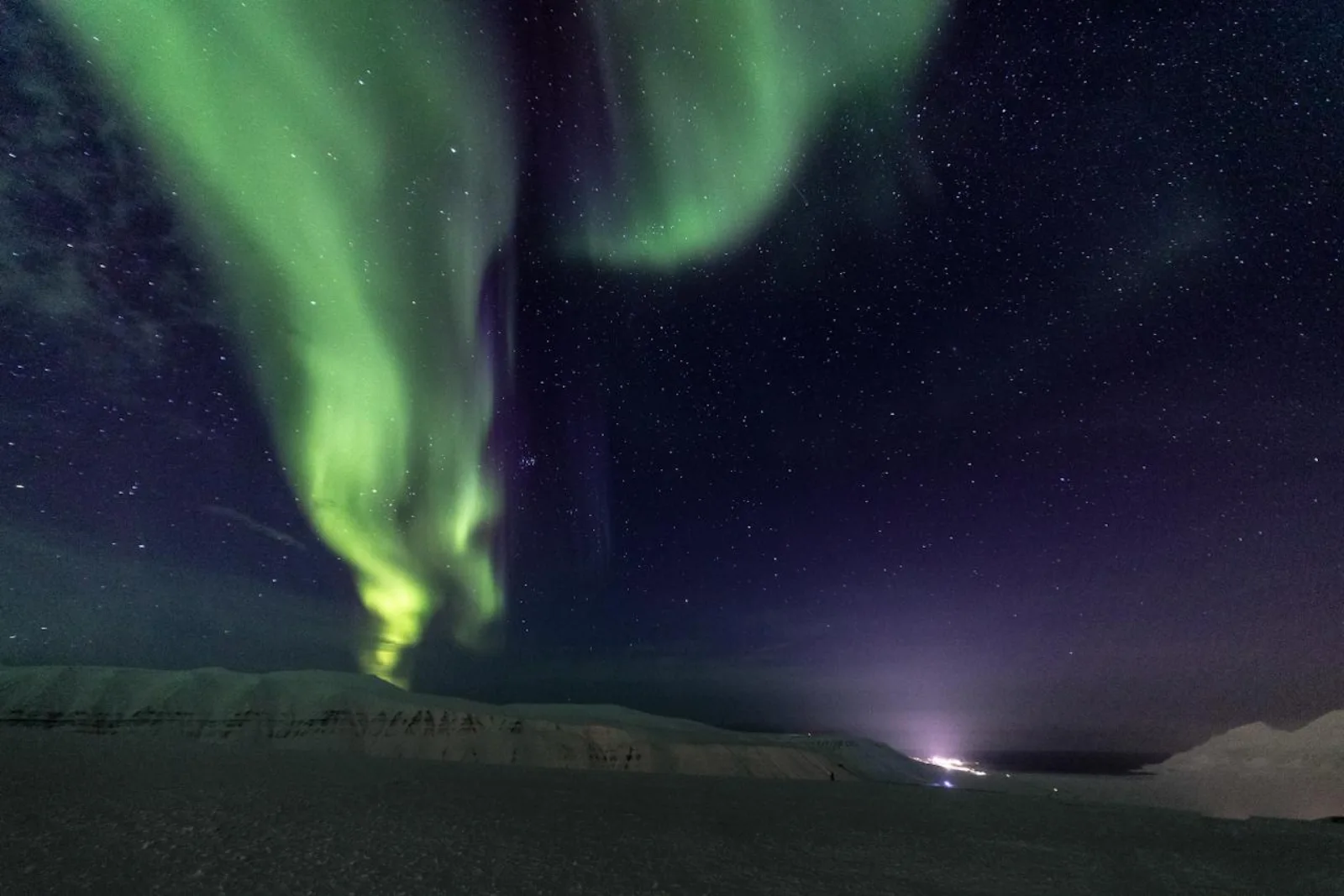 A green aurora band above Longyearbyen, the town lights visible along the fjord