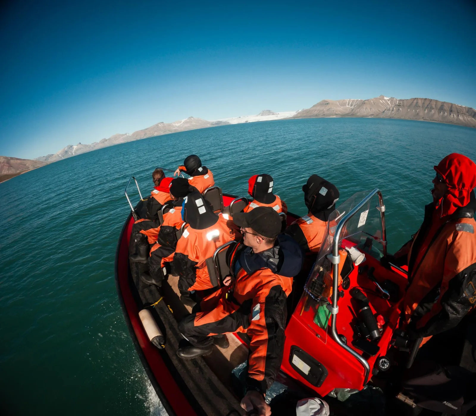 Guests in survival suits aboard the RIB crossing Isfjorden under a clear sky
