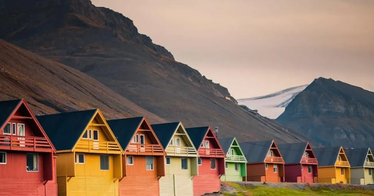 Row of colourful wooden houses in Longyearbyen below dark Svalbard mountains with a snowfield behind