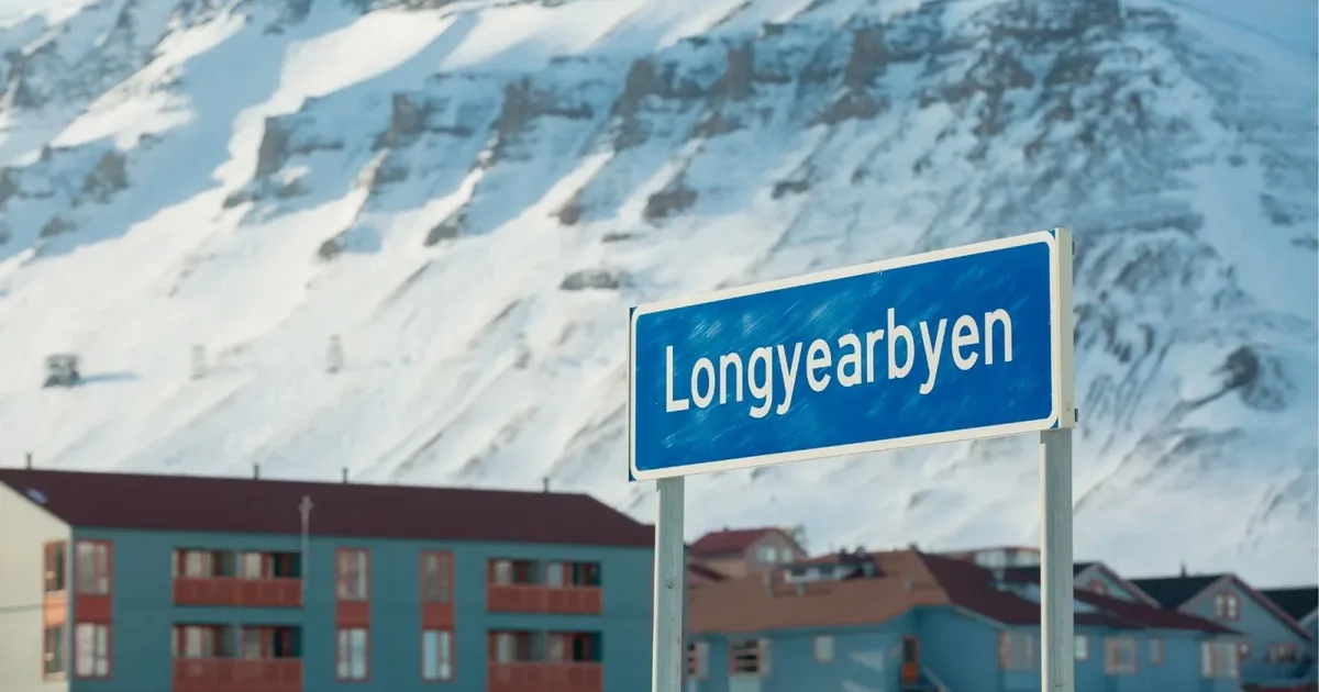 The Longyearbyen town sign in front of apartment buildings under snowy mountains
