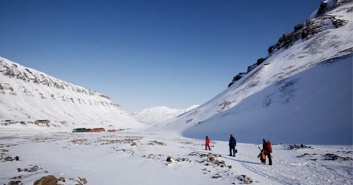 Three people walking across a snow-covered Svalbard valley beneath a clear blue sky